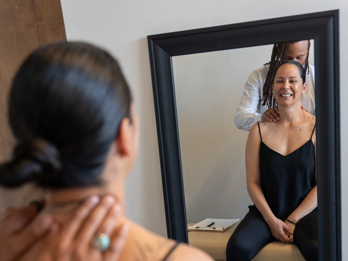 Dr. Jamal Früster examining a smiling patient’s neck as she sits on the exam table at Alma Sana Chiropractic Studio in Tucson